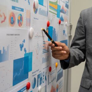 A male businessman explains graphs on a board during a meeting. He discusses marketing and finance