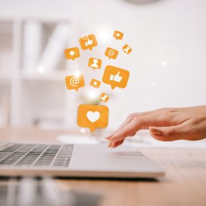 cropped view of businesswoman typing on laptop at workplace with multimedia icons