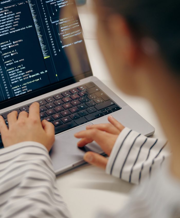 Close up of female software engineer writing code on laptop with screens setup in coworking